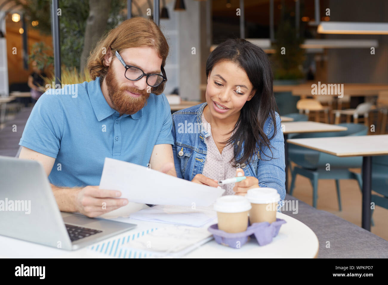 Junge Geschäftsleute in Freizeitkleidung zusammen sitzen am Tisch mit Laptop lesen und diskutieren business Vertrag im Cafe Stockfoto