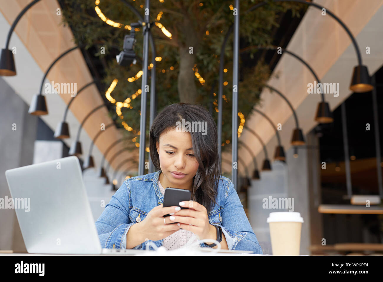 Junge Geschäftsfrau in Freizeitkleidung sitzen am Tisch mit Laptop und Handy im Restaurant Stockfoto