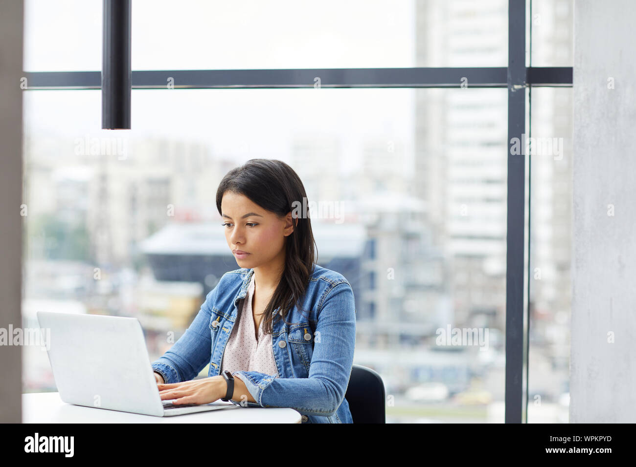 Junge seriöse Geschäftsfrau in Freizeitkleidung online Arbeiten am Laptop im modernen Büro Stockfoto