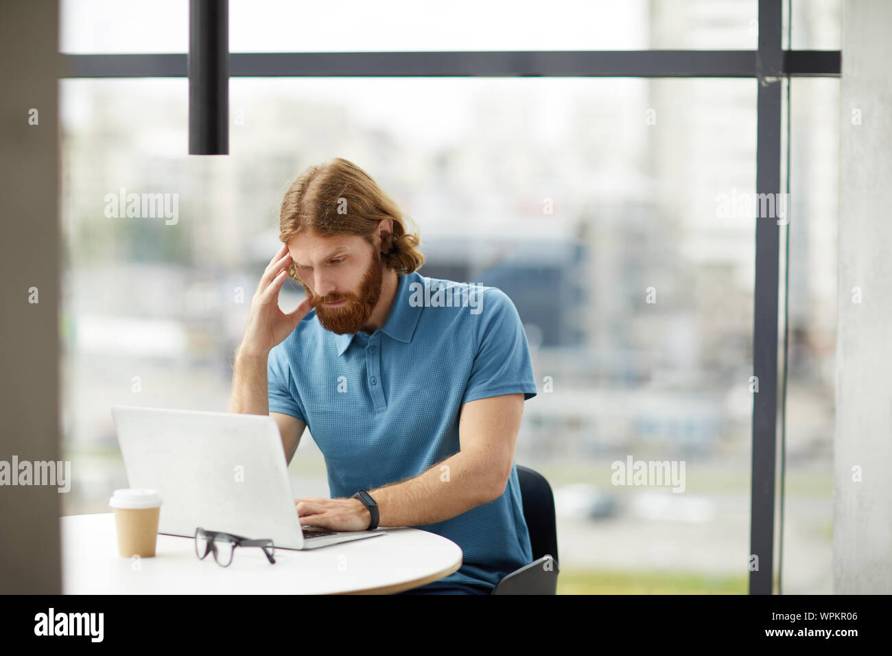 Junge Bartgeier Geschäftsmann in Freizeitkleidung sitzen am Tisch und die Konzentration auf seine online Arbeiten am Laptop im Büro Stockfoto