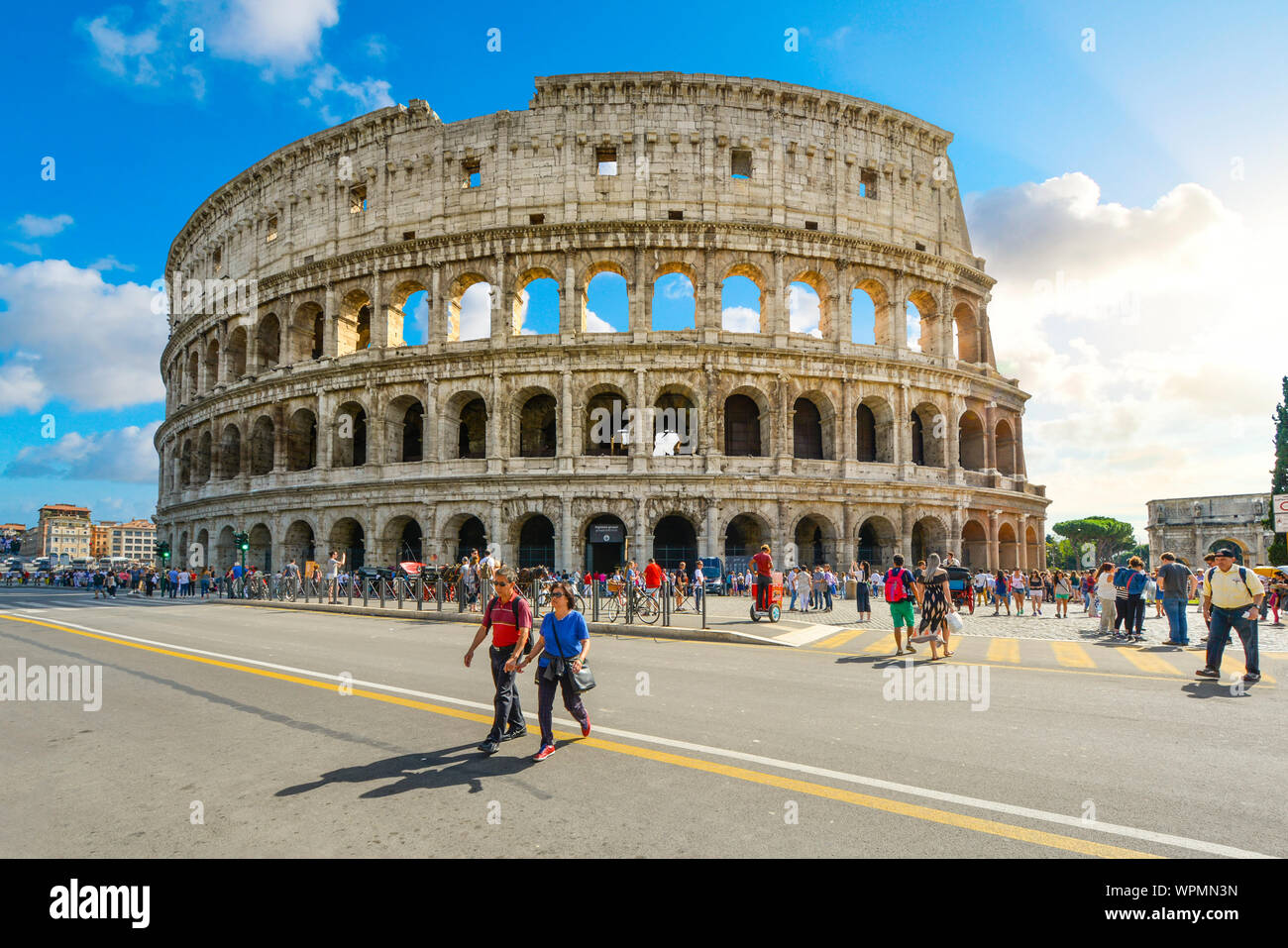 Die antike Arena, das Kolosseum von Rom in Italien an einem Sommertag mit Touristen, die über die Via dei Fori Imperiali Stockfoto