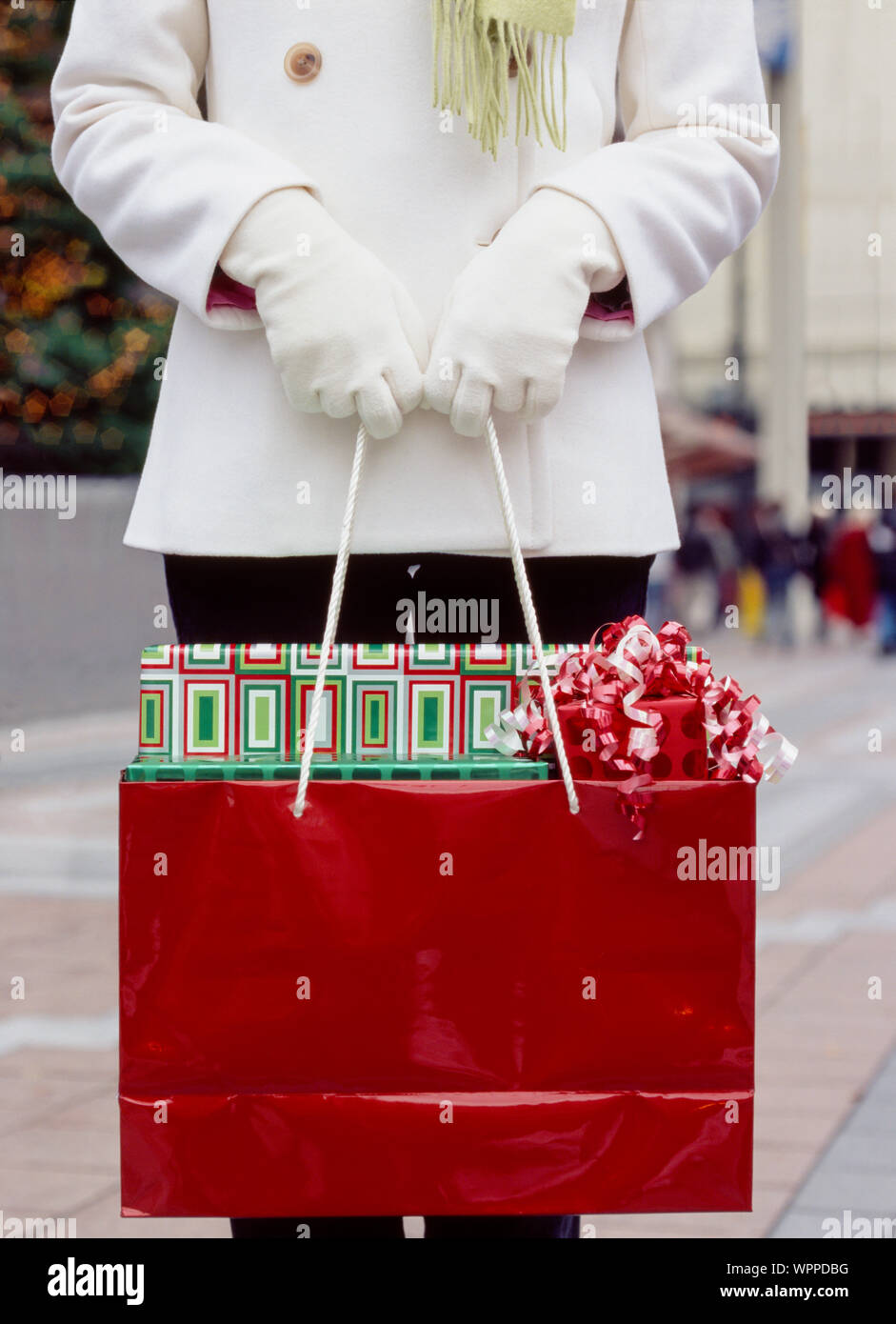 Frau in Weiß Wollmantel und Handschuhe holding Einkaufstasche mit verpackt Weihnachten Geschenke Geschenke. Leute Weihnachten Shopping in der Stadt. Stockfoto