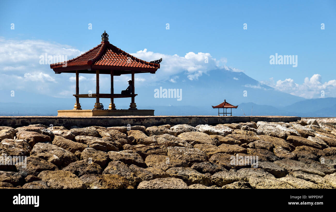 Silhouette der Mann am helllichten Tag eine Pause im Schatten unter einem traditionellen Unterkunft am Strand von Sanur, Bali, Indonesien. Stockfoto