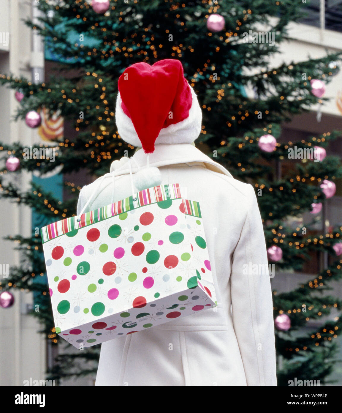 Frau in Weiß Wollmantel und Santa hat Holding Einkaufstasche mit Weihnachtsbaum im Hintergrund. Urlaub, Christmas shopping in der Stadt Geschenke pre Stockfoto