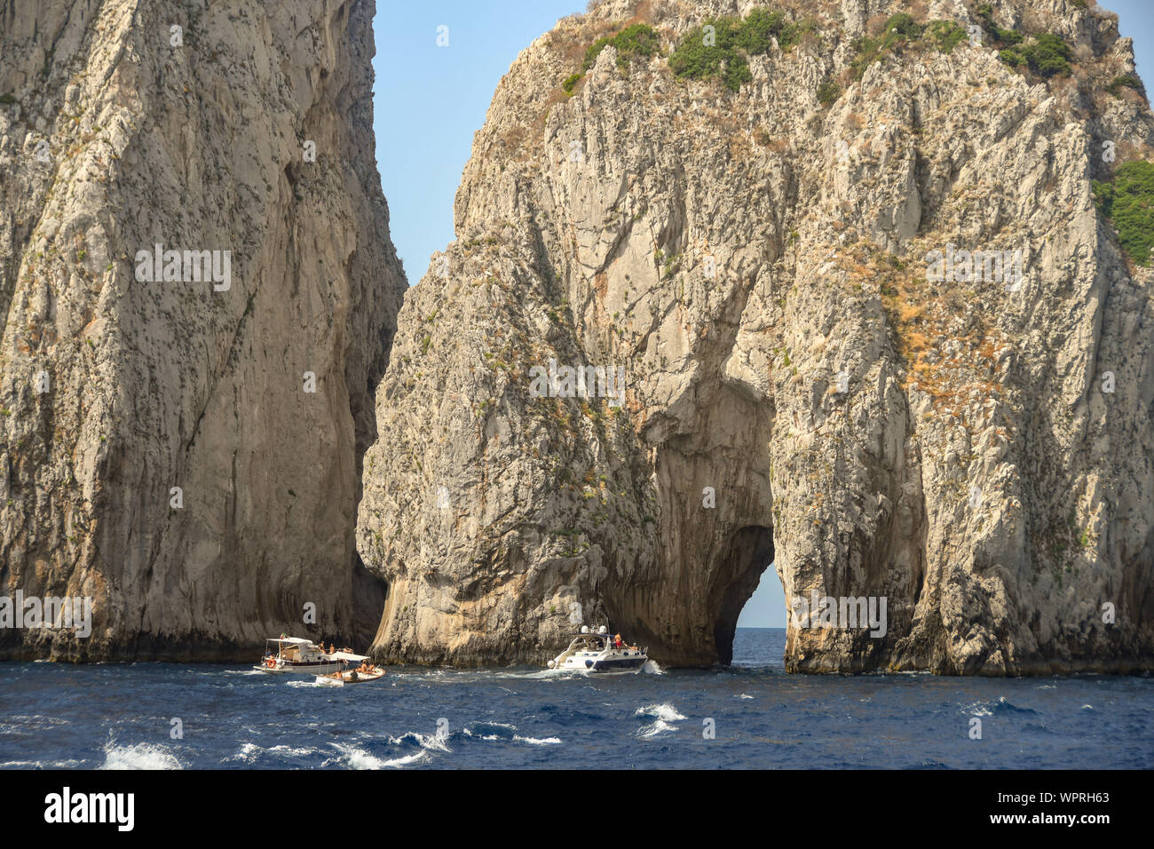 Insel Capri, Italien - AUGUST 2019: Die Faraglioni Felsen an der Küste von Capri. Kleine Boote sind durch den Arch. Stockfoto