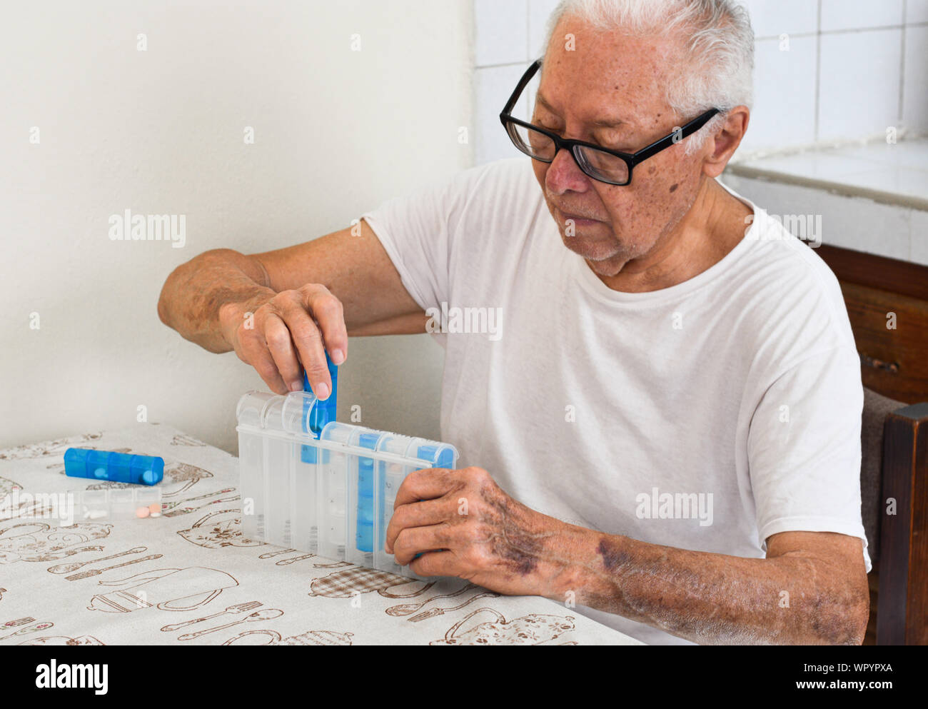 Älterer mexikanischer Mann, der seine Medikamente in einen Tablettenorganisator einsortierte Stockfoto