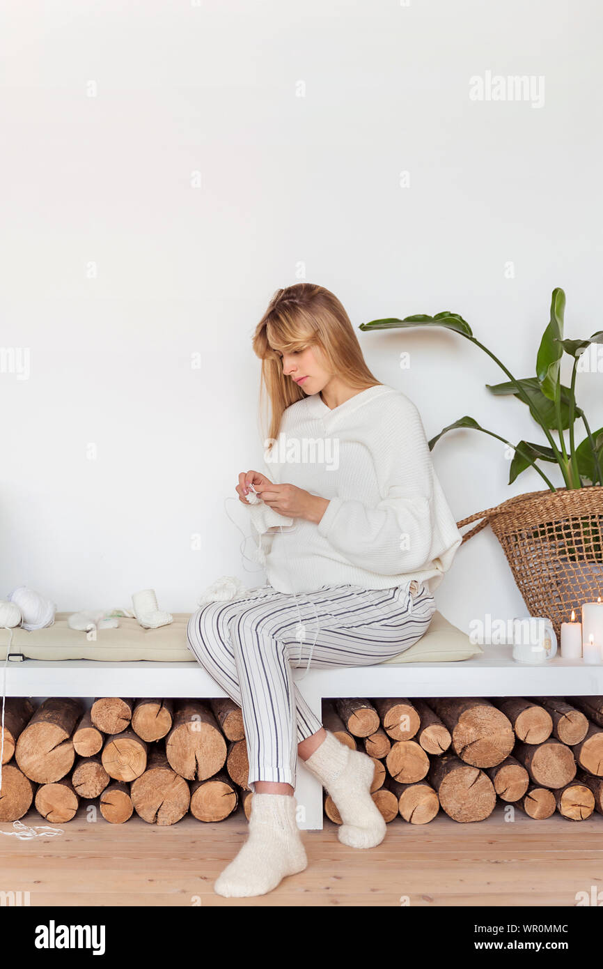 Blond strickt Socken für ein Neugeborenes sitzt auf einem weichen Kissen in einer gemütlichen Skandinavischen Interieur Stockfoto