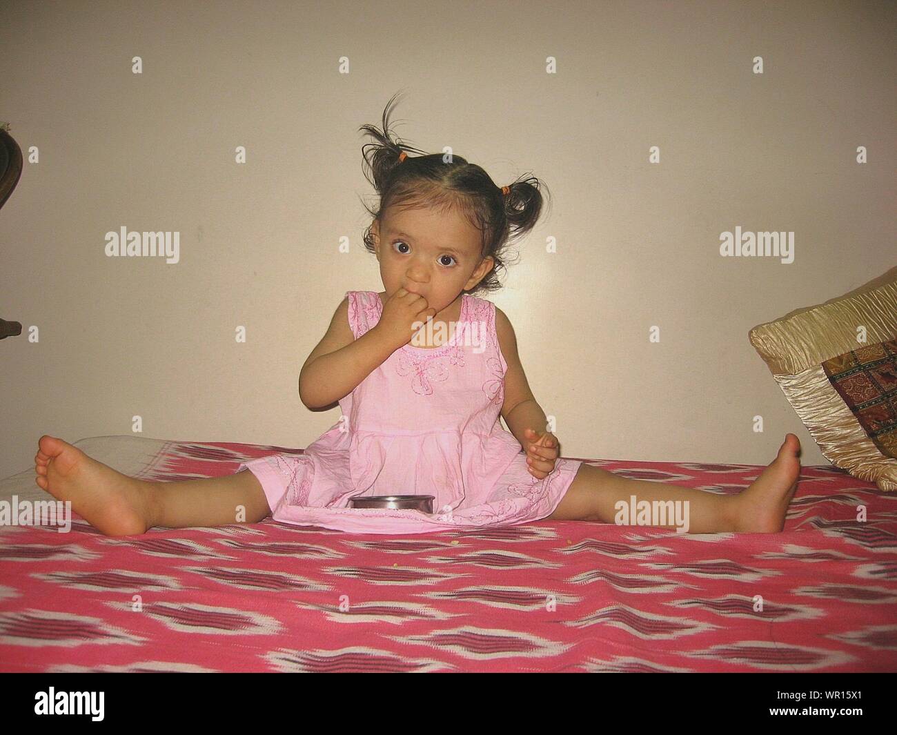 Portrait Von Mädchen Sitzen Mit Breitbeinig Auf Dem Bett Beim Essen Gegen Die Wand 9240