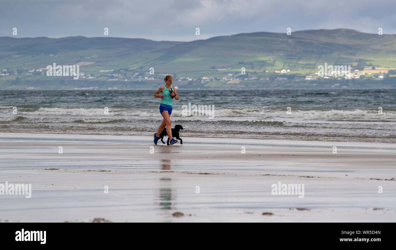 Frau joggen auf benone Strand mit ihrem Hund, Nordirland, Großbritannien. Stockfoto