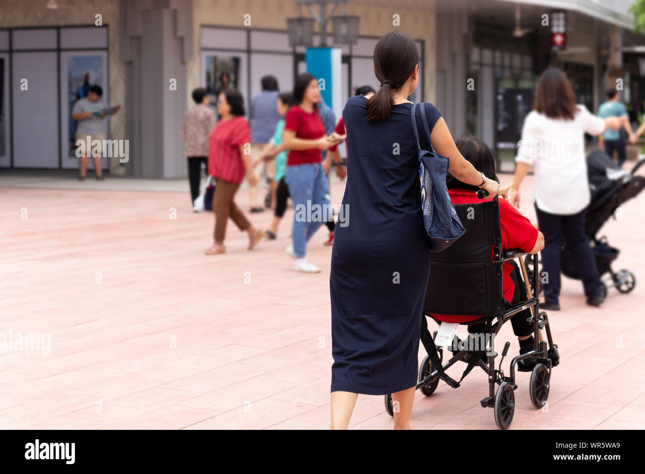 Tochter ihre Mutter im Rollstuhl spazieren Sie entlang der Shopping Mall. Stockfoto