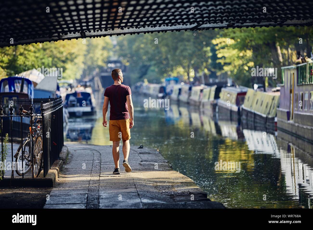 Junger Mann zu Fuß an der Strandpromenade von Regents Canal mit Booten. Little Venice in London, Vereinigtes Königreich. Stockfoto