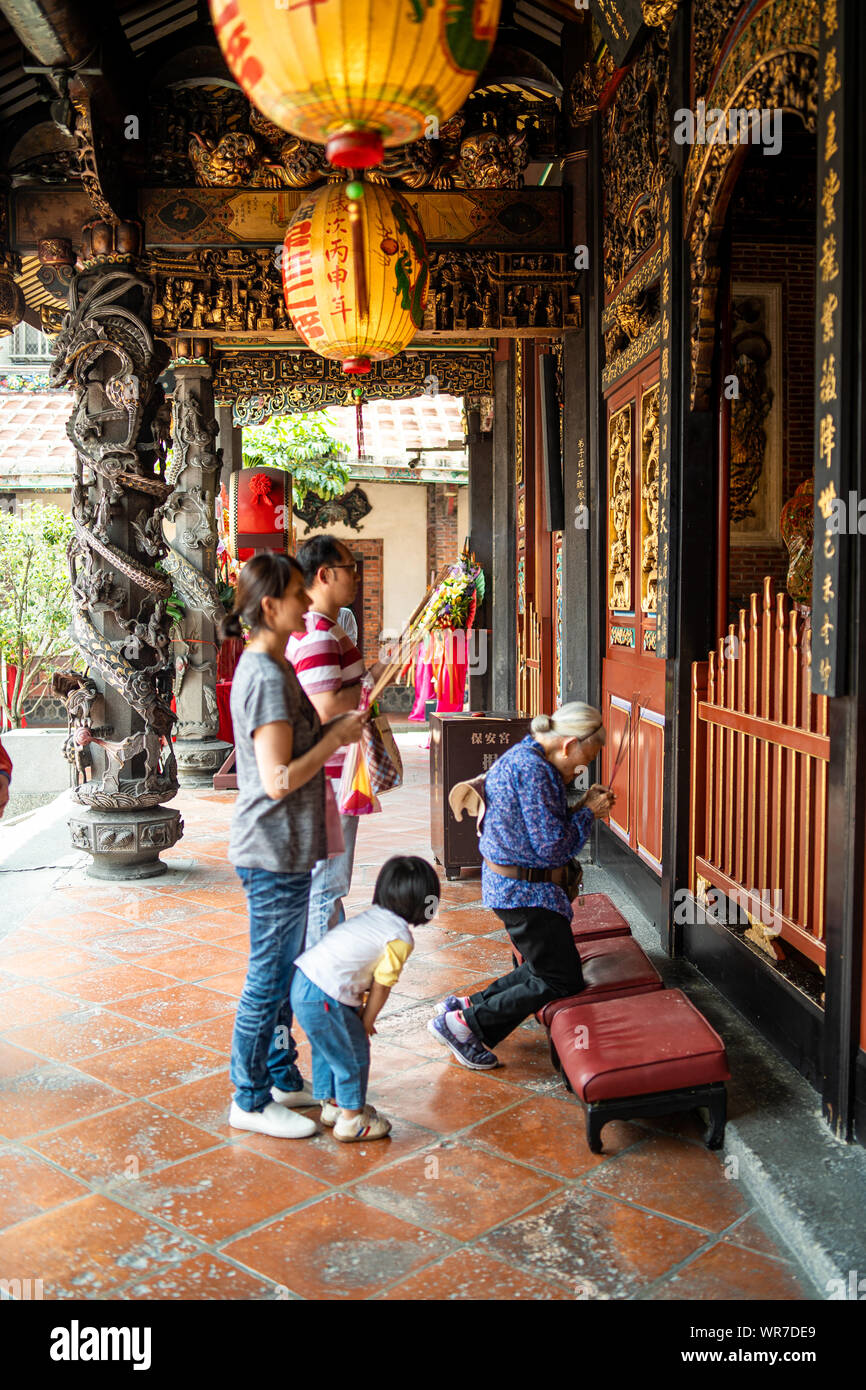 Taipei, Taiwan: Familie mit Kind und Großmutter Gebet an alten Dalongdong Baoan Tempel neben Spalten mit Drachen Ornamente Stockfoto