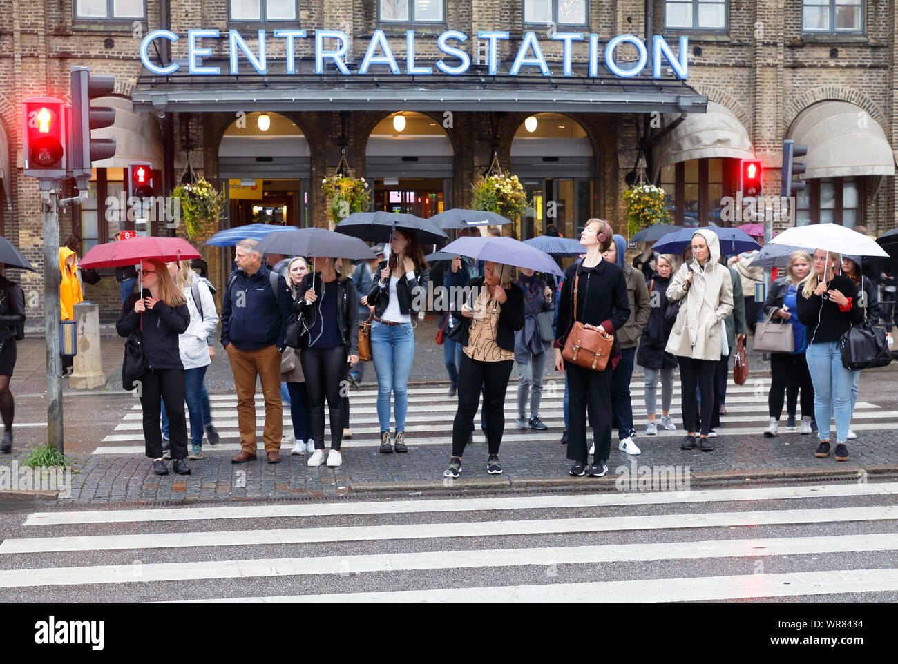 Göteborg, Schweden - 3. September 2019: Menschen beim Zebrastreifen vor dem Hauptbahnhof warten mit umbrrallas im Regen für ein grünes Licht. Stockfoto
