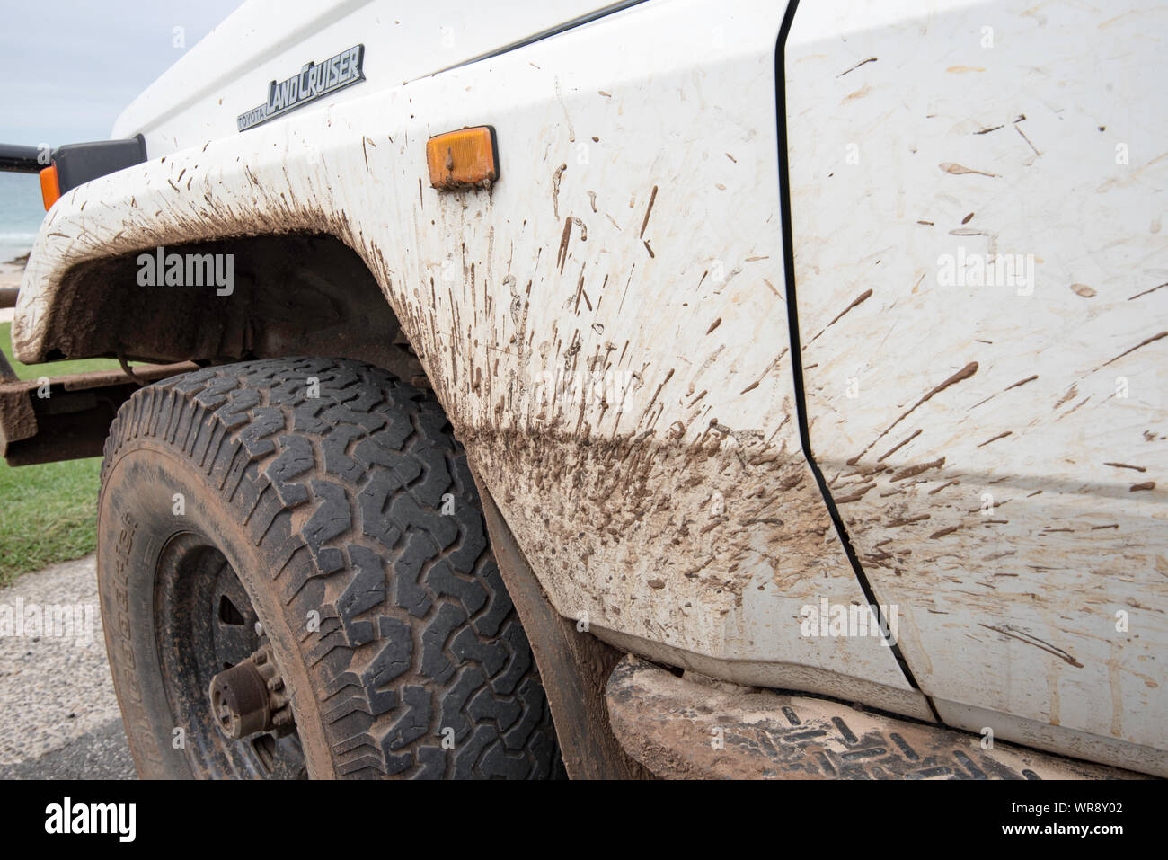 Vorne auf der Beifahrerseite vor einer weißen 4WD Toyota Land Cruiser Troop Carrier (aka Troopie) geparkt und mit Schlamm bespritzt Stockfoto