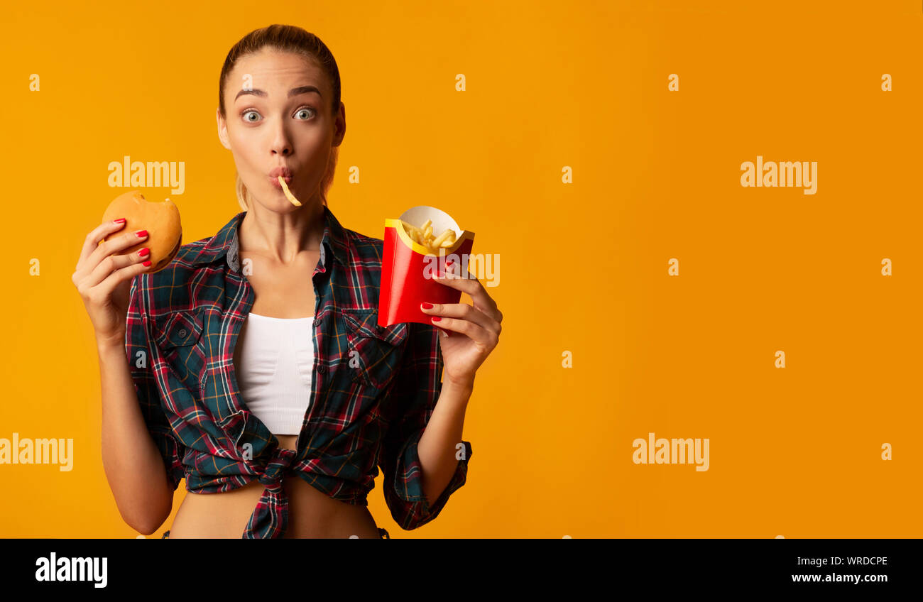 Mädchen Essen Burger und Pommes Frites auf gelbem Hintergrund Stockfoto
