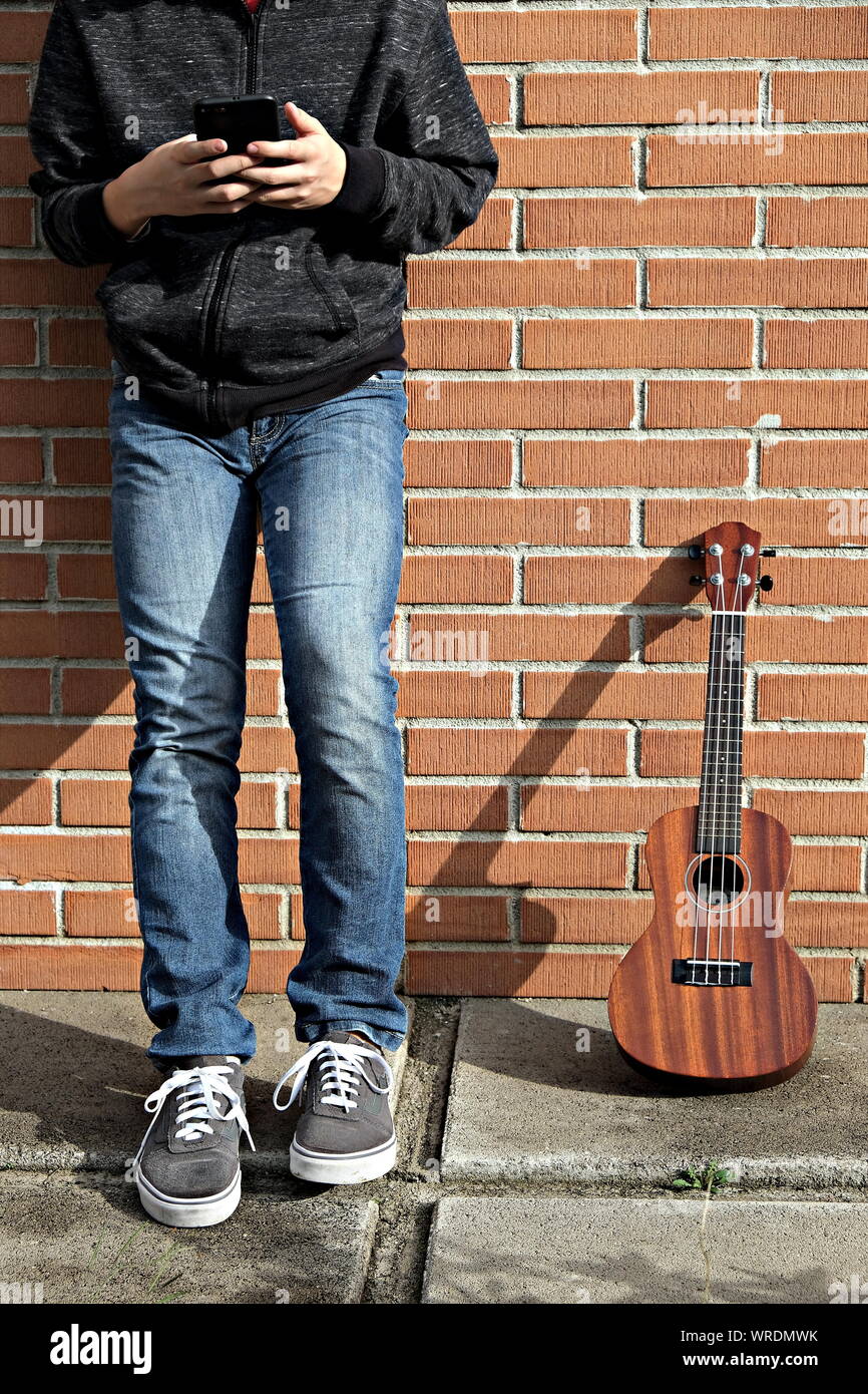 Junge ukulele Player auf Pause Kontrolle des Smartphones Stockfoto