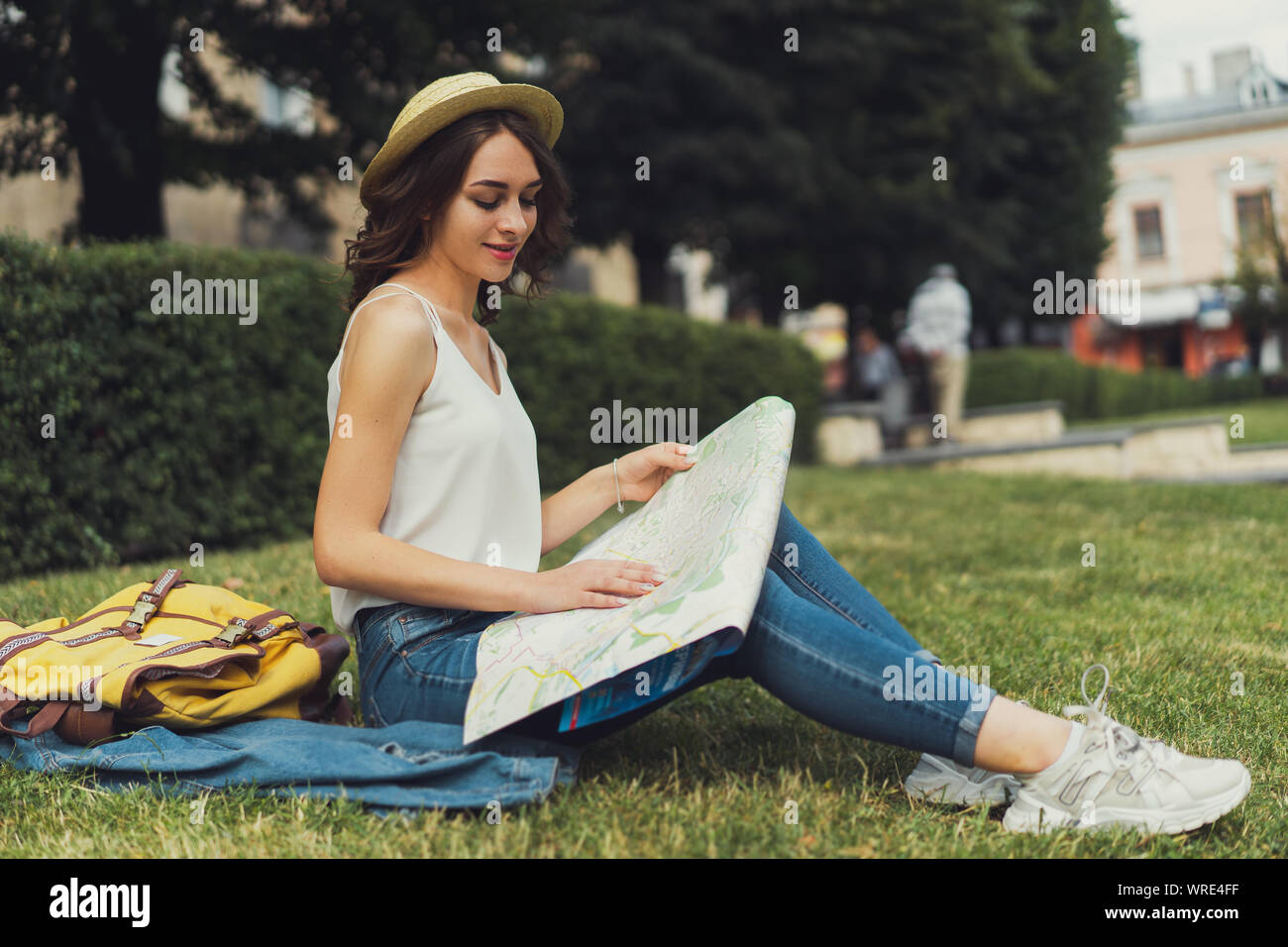 Schöne junge Frau sitzt auf Gras genießen Sie sonnige Tag im Park. Mit einem sanften Lächeln auf den Lippen. Eine Karte in die Hände. Stockfoto