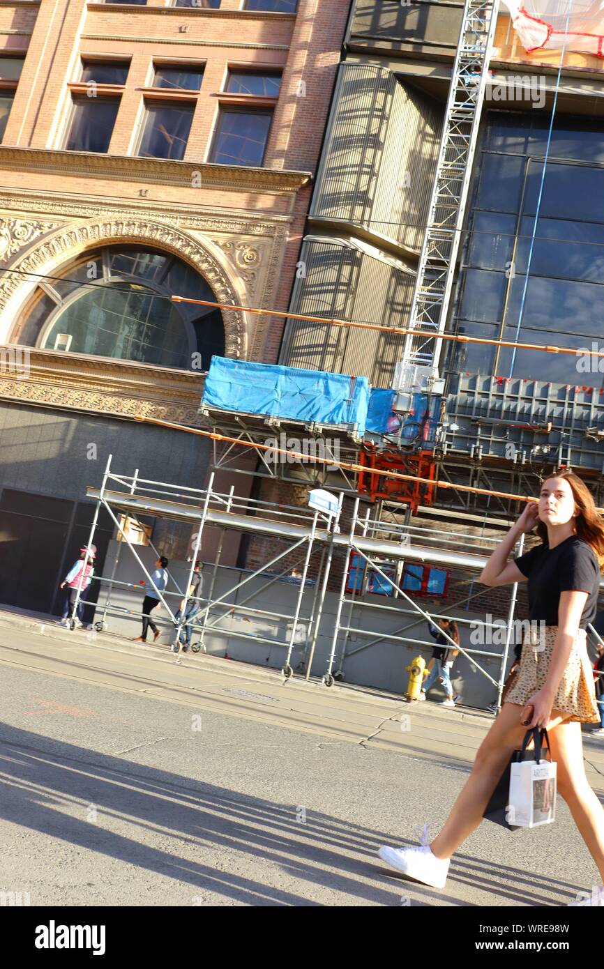 Eine junge Frau in kurzen Rock und weisse Turnschuhe trägt eine Einkaufstasche in der Queen Street in der Innenstadt von Toronto Stockfoto