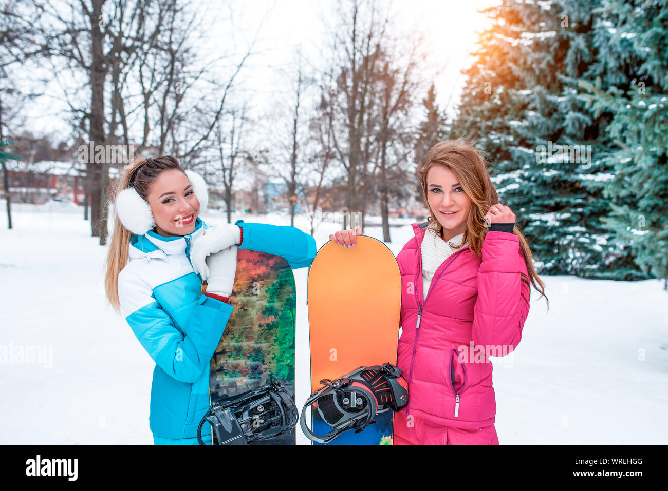 Zwei Mädchen Freundinnen winter Hintergrund Schnee, Grüne fichte, Boards Snowboarden. Glückliche Lächeln, Spaß freuen. Frauen Urlaub Freundschaft Stockfoto