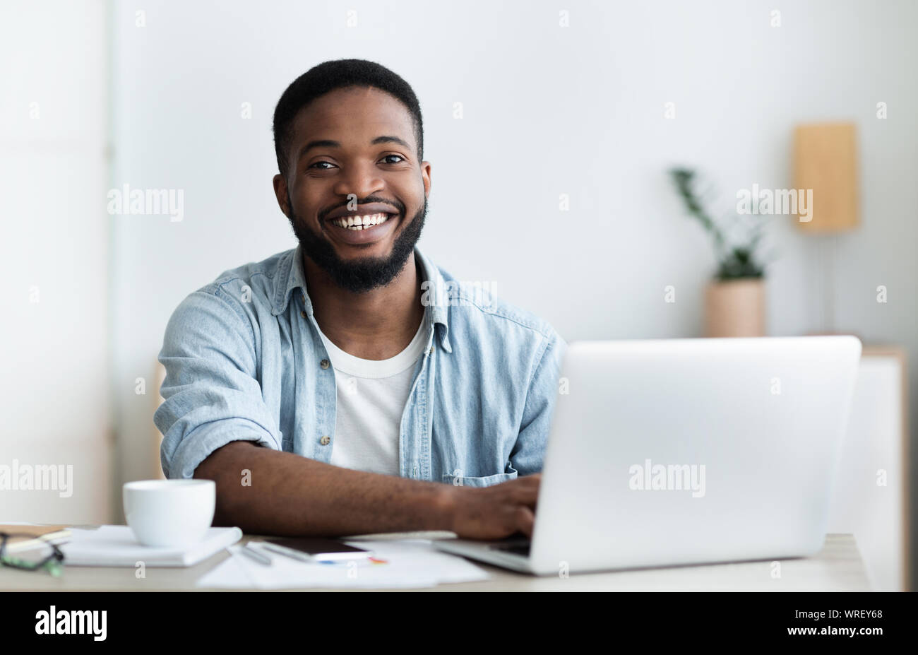 Afrikanische Arbeiter mit Laptop, lächelnd und trinken Kaffee im Büro Stockfoto