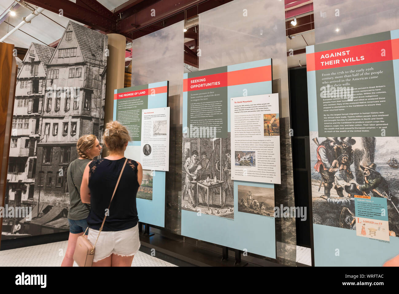 Frauen-Museum, Rückansicht von zwei jungen Frauentouristen, die auf eine Ausstellung im Ellis Island Museum, New York City, USA, blicken. Stockfoto