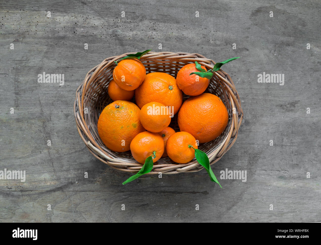 Mandarinen mit Blättern in weiß Warenkorb auf rustikalem Holz Hintergrund. Citrus nur aus dem tree.Organic veg Essen. Winter Früchte. Stockfoto