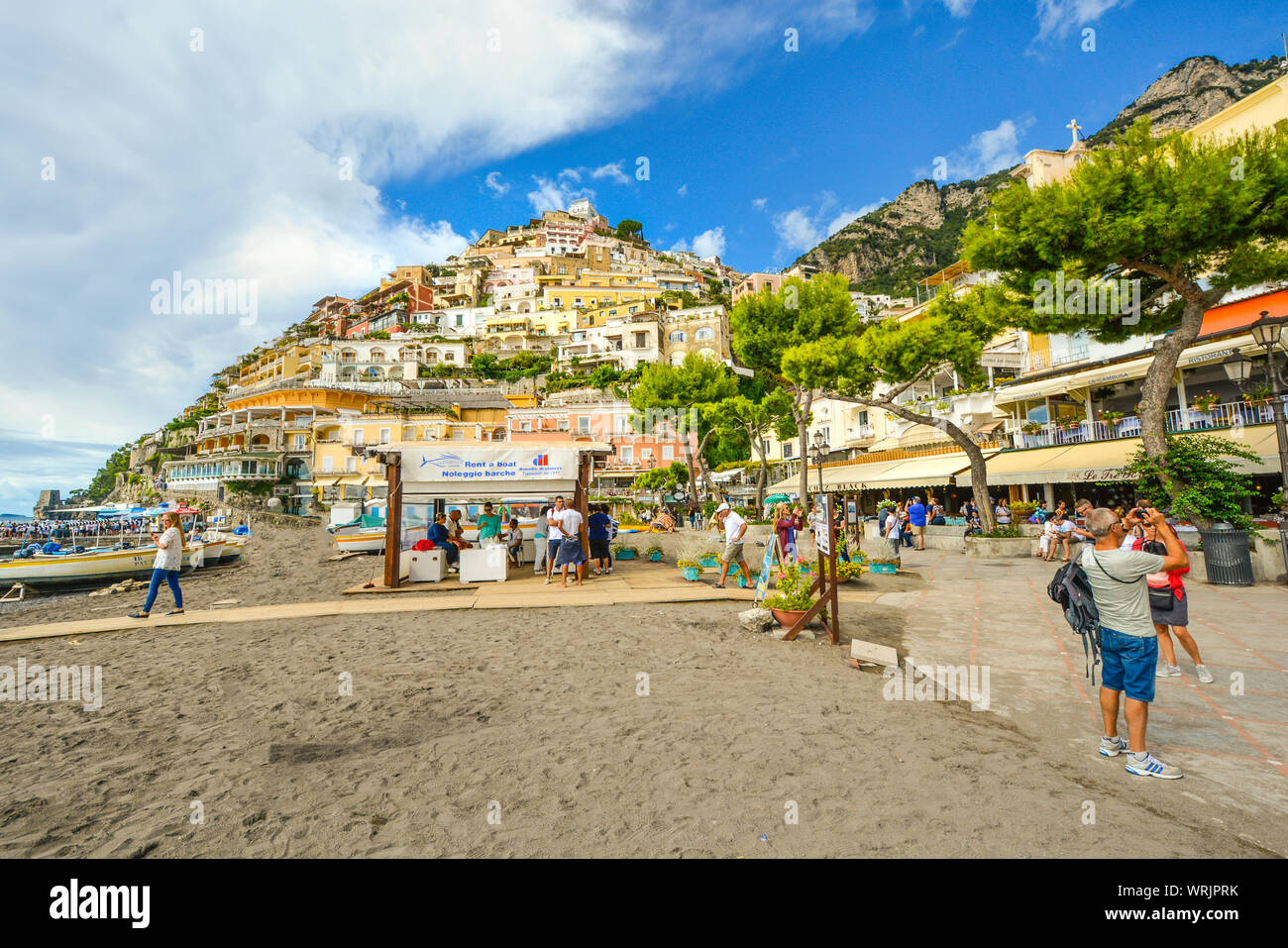 Touristen zu Fuß der Promenade und Sandstrand, Cafés und Geschäfte in der Küstenstadt Positano Italien an der Amalfi Küste des Mittelmeers Stockfoto