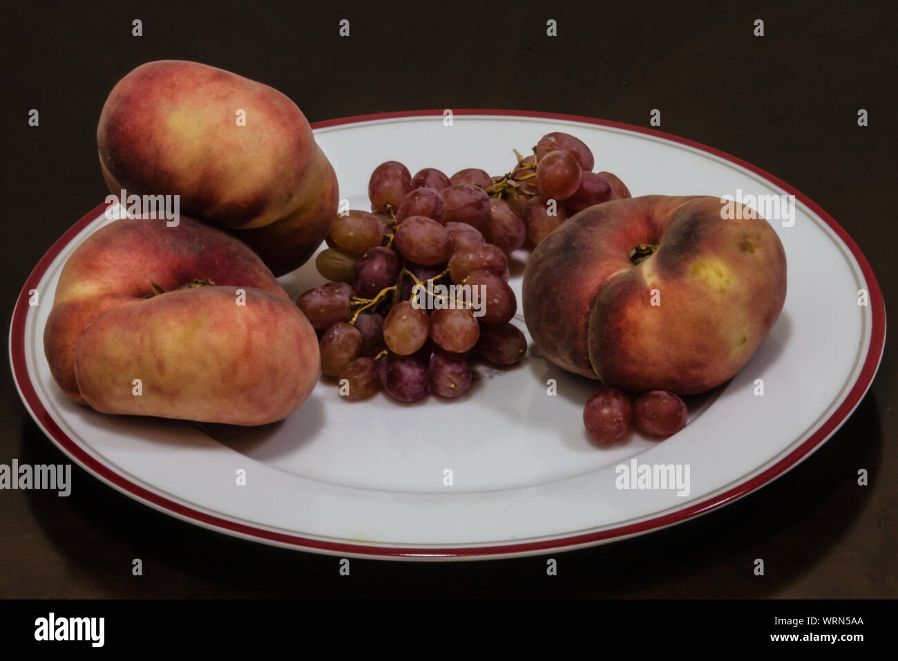 Flache Pfirsich (Prunus Persica var. platycarpa) und rote Traube auf weißem Schild Stockfoto