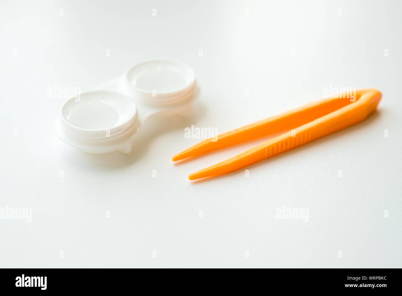Zubehör für die richtige Verwendung von Kontaktlinsen: Gehäuse und orangefarbene Pinzette auf hellweißem Hintergrund. Sichere Sehkorrektur. Selektiver Fokus. Stockfoto