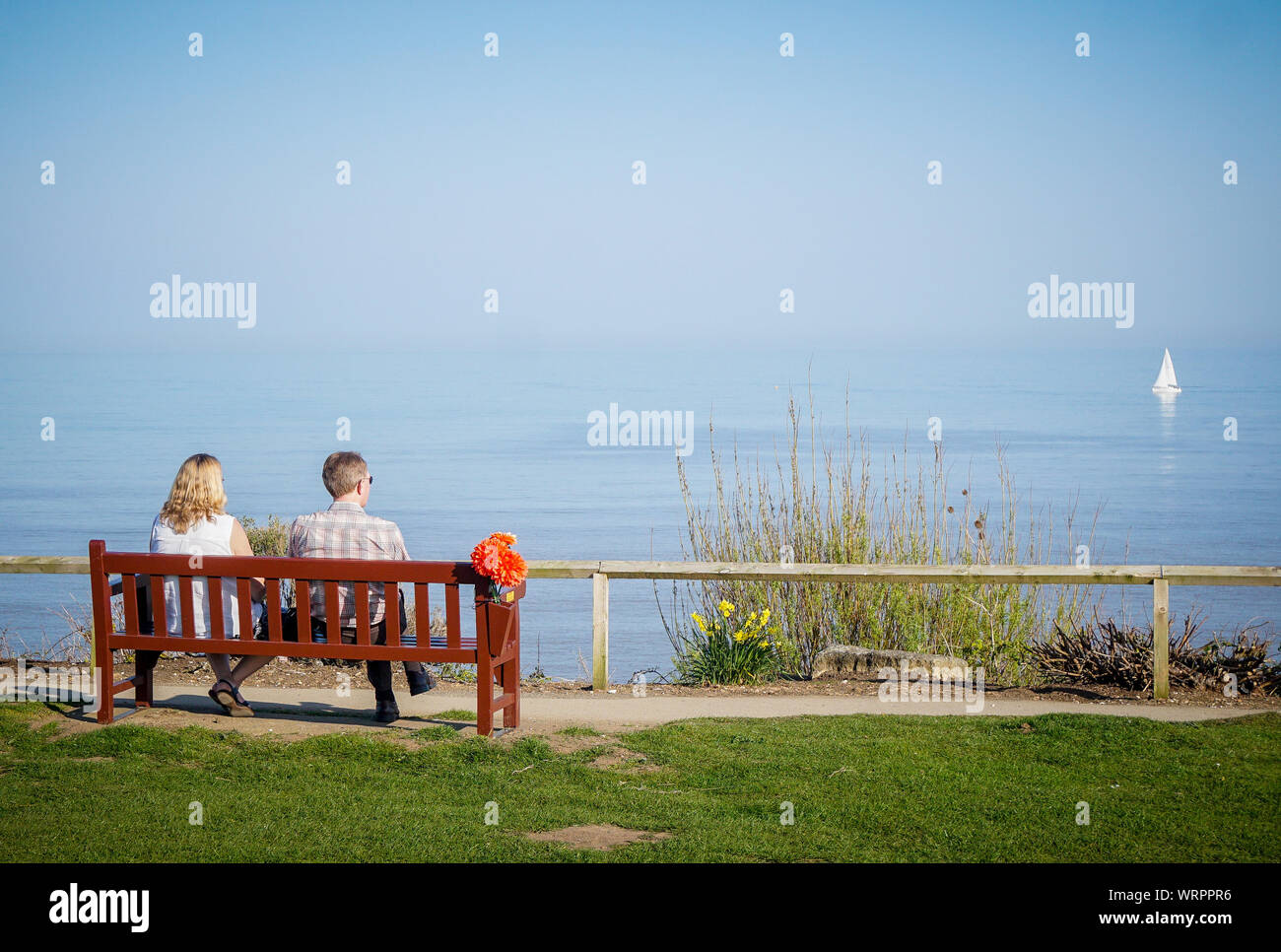 Ein paar sitzen auf einer Bank, wie sie es für ein Segelboot vorbei am Strand von Bridlington (Foto von Ioannis Alexopoulos/Alamy) Stockfoto