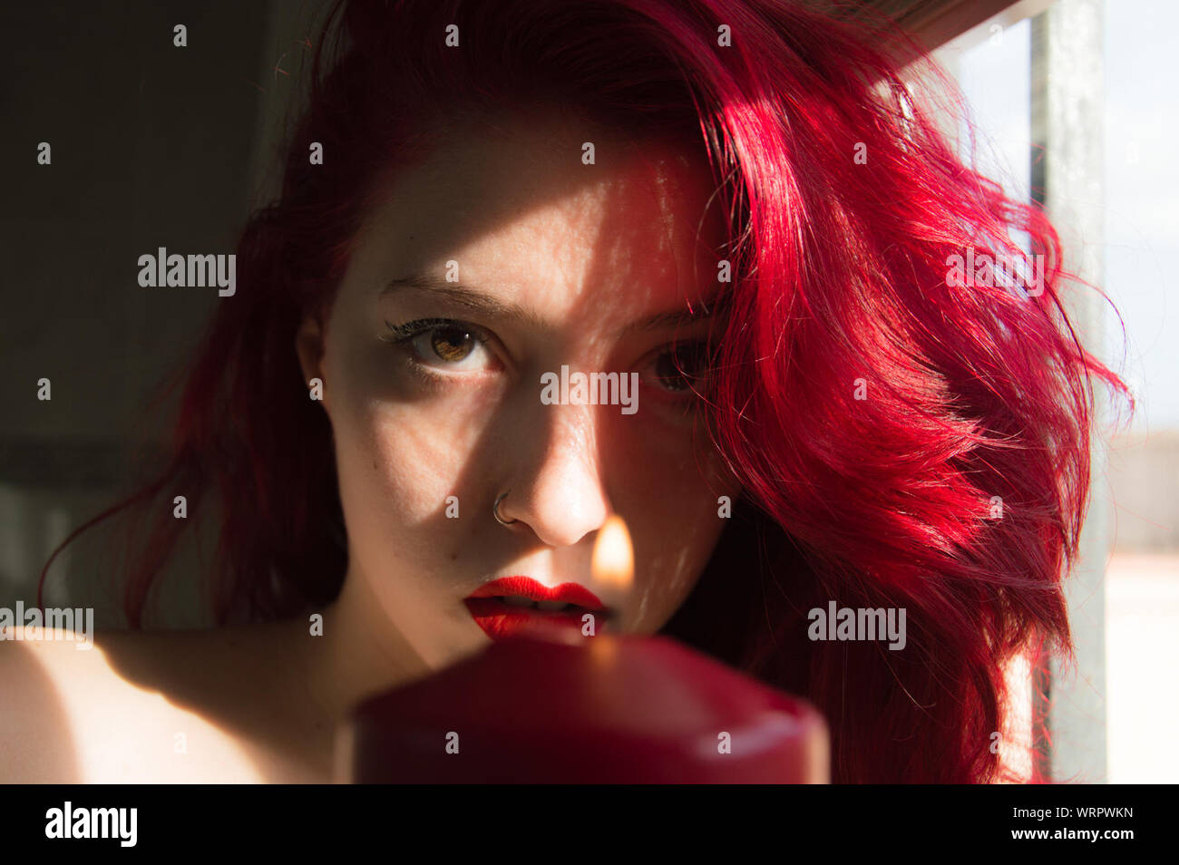 Portrait schöne Frau mit rot gefärbten Haaren durch die Fenster zu Hause Stockfoto