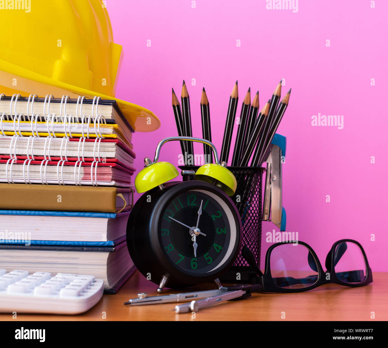 Close up Lehrmaterialien auf Schreibtisch aus Holz, Bau Helm, Stapel von Buch, Taschenrechner, Stifte, Uhr, Trennwände, Hefter und Gläser isoliert Stockfoto