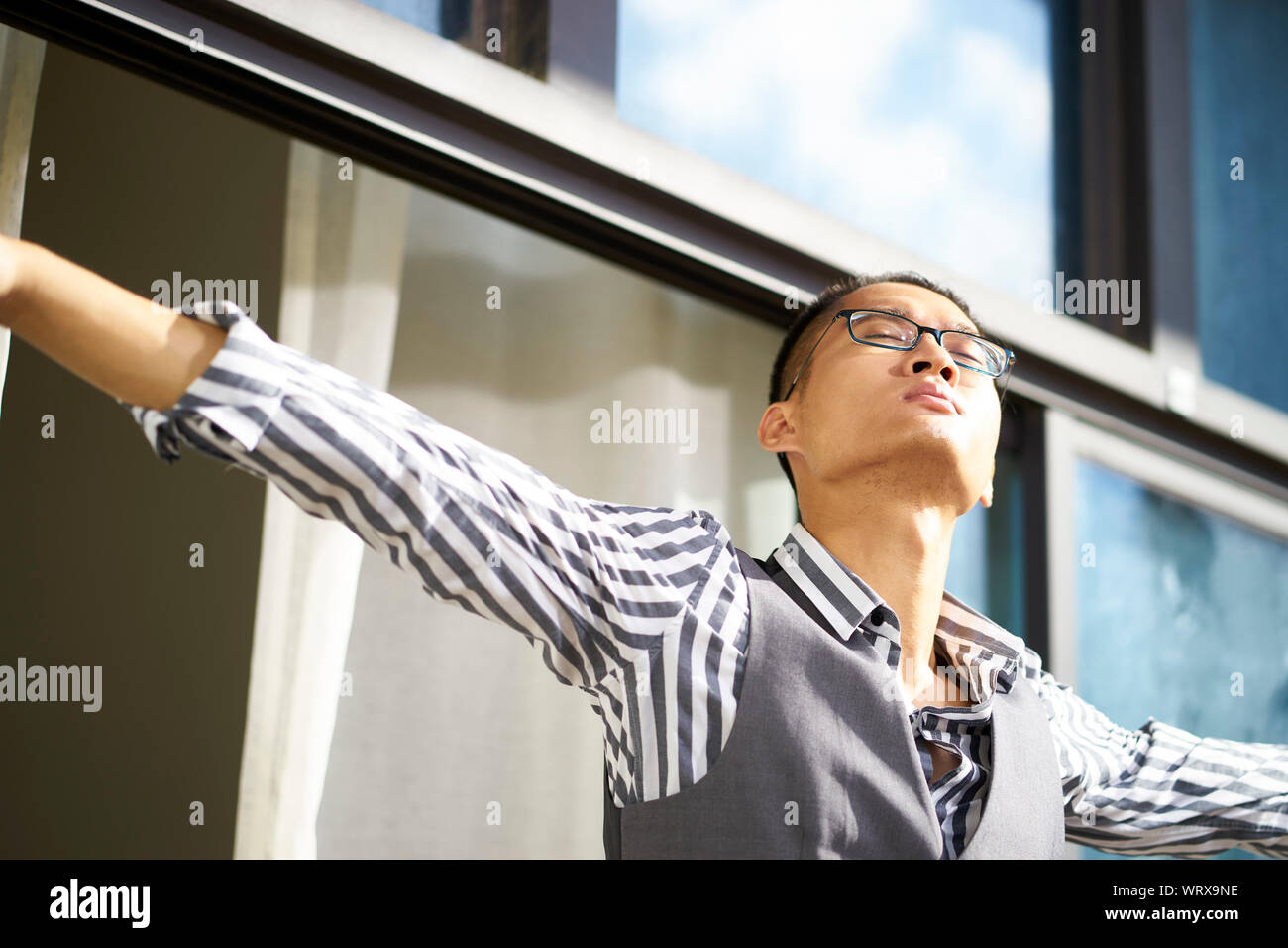 Jungen asiatischen Mann stand auf der Terrasse genießen Sie die frische Luft mit offenen Armen Stockfoto