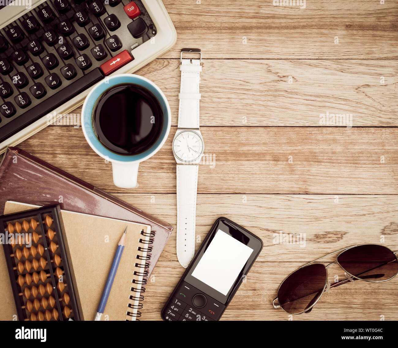 Büro Schreibtisch Hintergrund. Kaffee, Notizblock, Bleistift, Armbanduhr, Buch, Handy, Sonnenbrille, Abacus und Schreibmaschine auf vintage Schreibtisch aus Holz Stockfoto