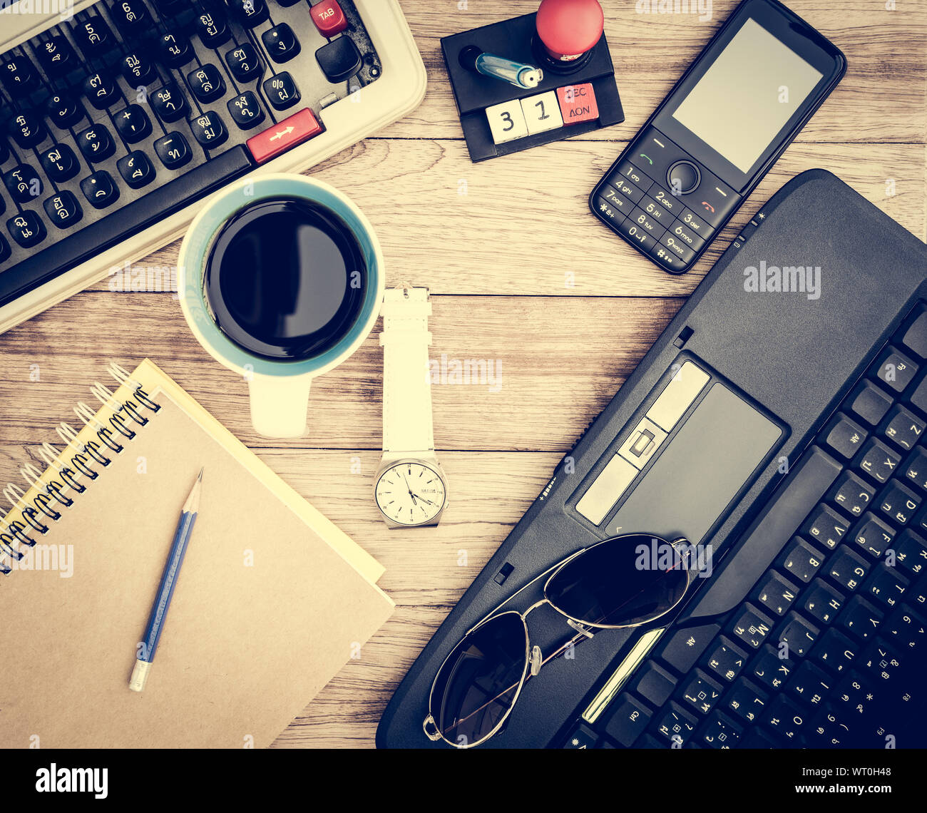 Büro Schreibtisch Hintergrund. Kaffee, Notizblock, Bleistift, Armbanduhr, Handy, Laptop, Sonnenbrille und Schreibmaschine auf vintage Schreibtisch aus Holz Stockfoto