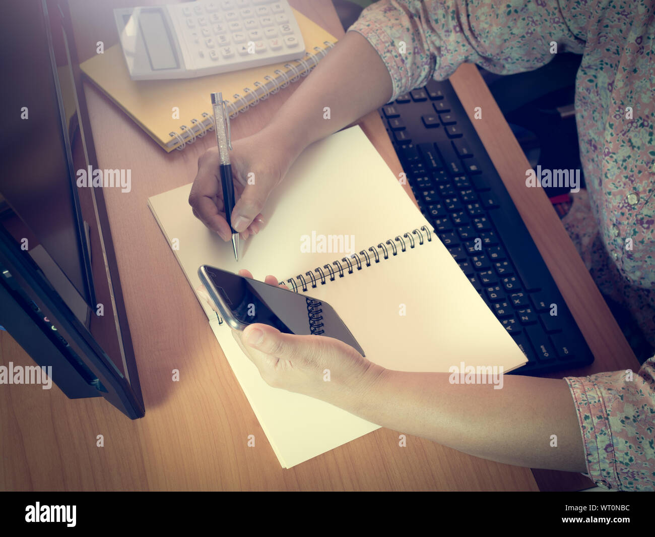 Hände von Frau Arbeiten am Schreibtisch, die eine Hand mit einem smart phone mit dem Schreiben auf Notepad, Geschäftskonzept. Stockfoto