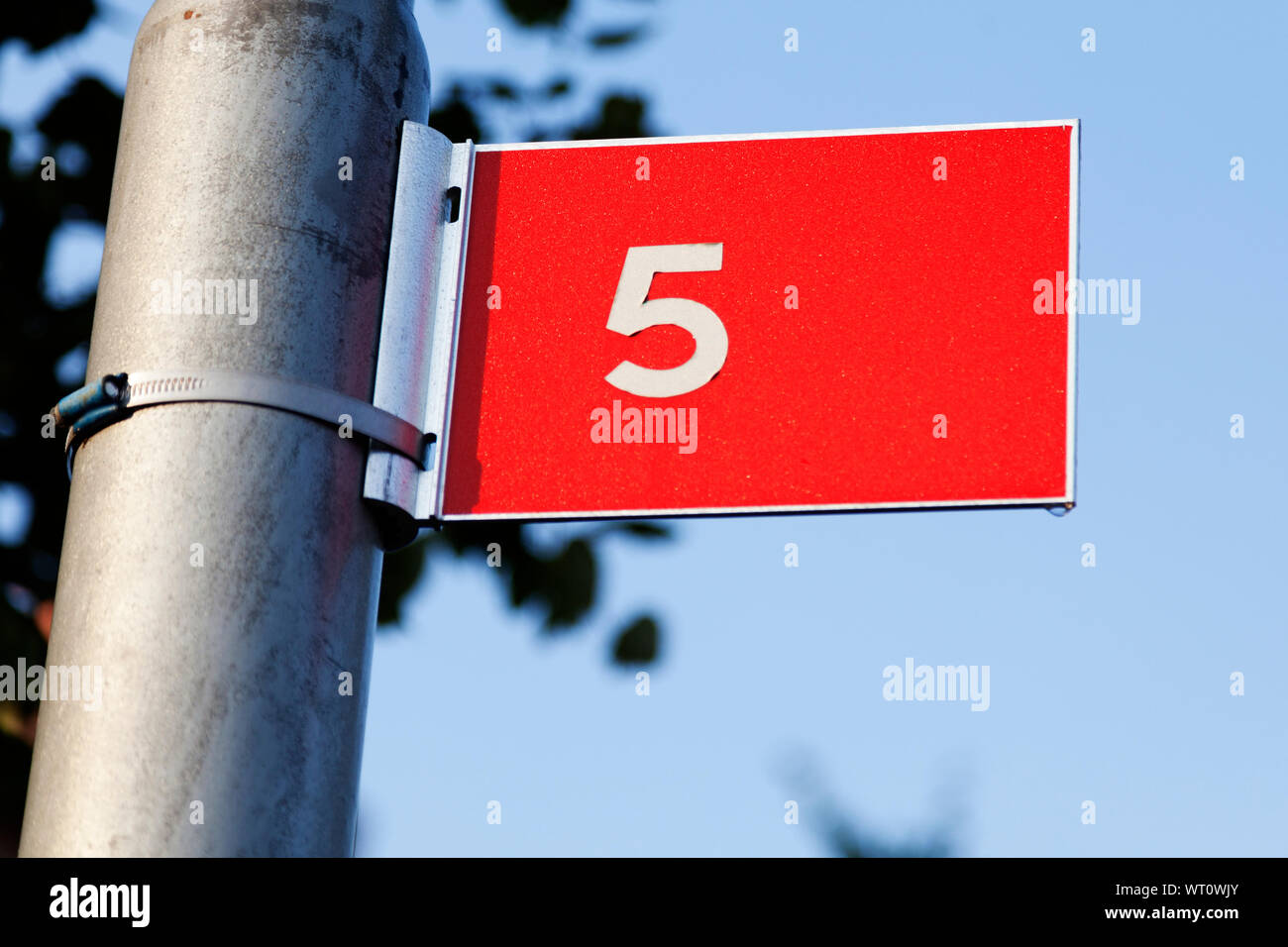 Rotes Schild mit weißem Text im Freien mit der Nummer Fünf, einen kleinen Tropfen Wasser an der Unterseite der Zeichen Stockfoto