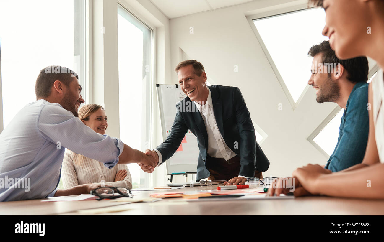 Herzlichen Glückwunsch zwei freundliche Kollegen die Hände schütteln und lächelnd, während im modernen Büro zu sitzen. Teamarbeit. Konferenz Stockfoto