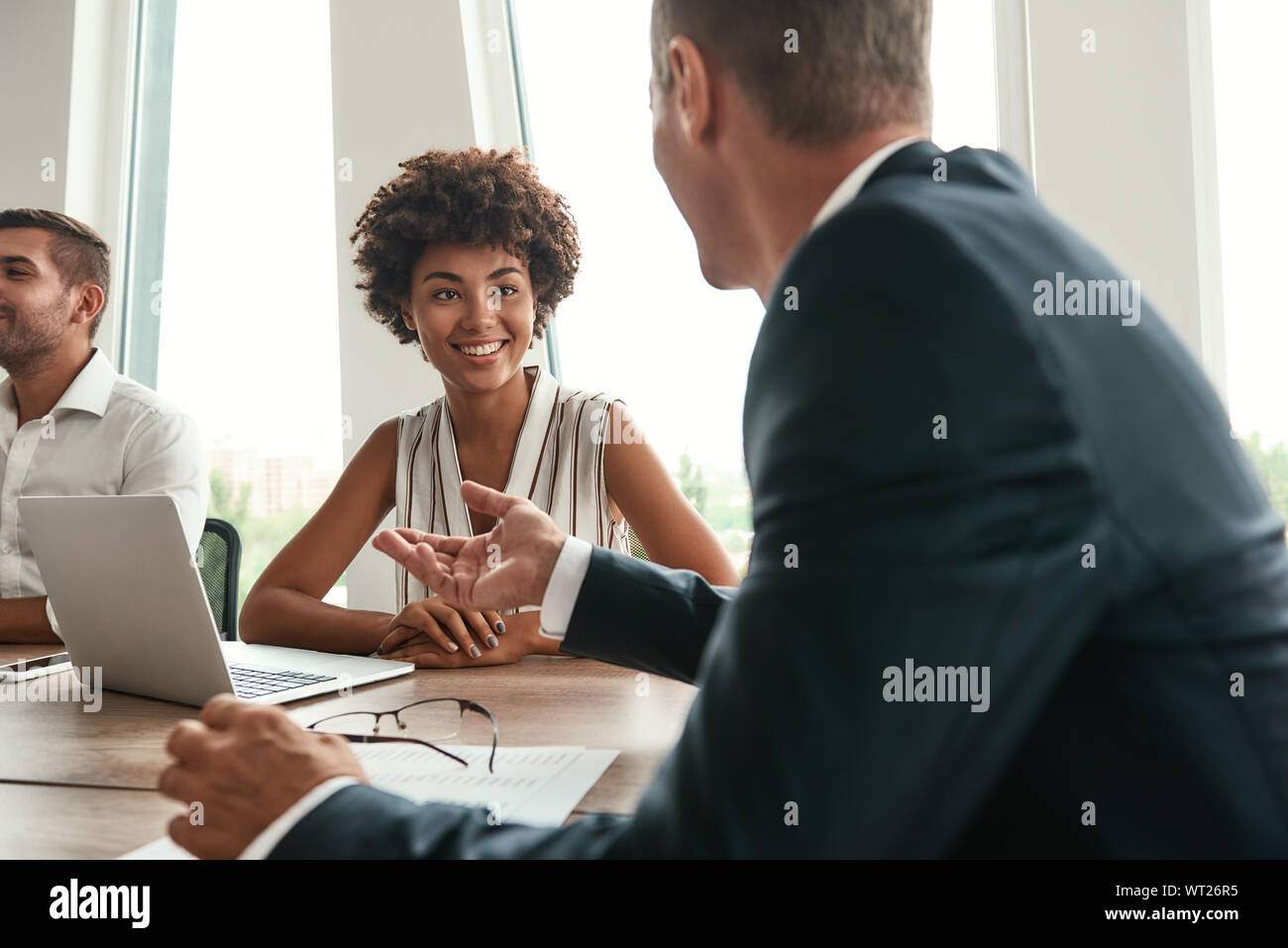 Multikulturelles Team. Junge und schöne afro-amerikanische Frau etwas diskutieren mit Kollegen und lächelnd, während im modernen Büro zu sitzen. Brainstorming. Business Meeting Stockfoto