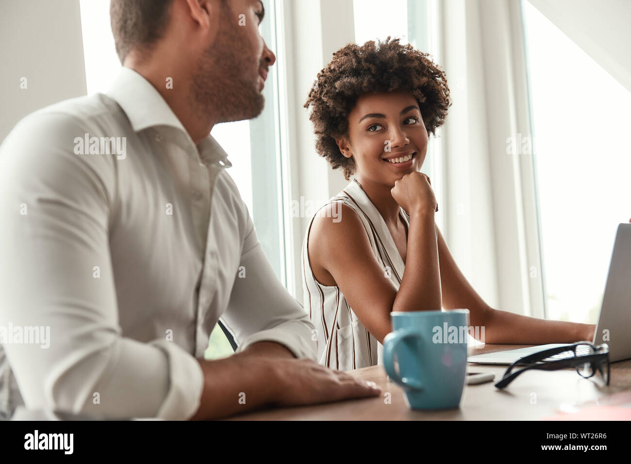 Neuen Arbeitstag. Junge und schöne afro-amerikanische Frau etwas diskutieren mit ihrem Kollegen, während im modernen Büro zu sitzen. Brainstorming. Business Meeting Stockfoto