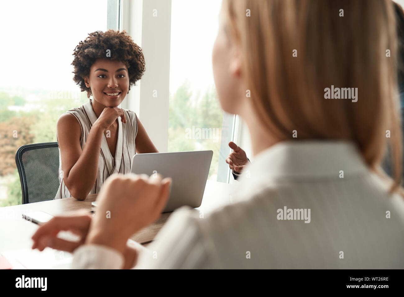 Teamarbeit. Junge und schöne afro-amerikanische Frau, die Arbeiten am Laptop und etwas diskutieren mit Kollegen, während im modernen Büro zu sitzen. Brainstorming. Business Meeting Stockfoto