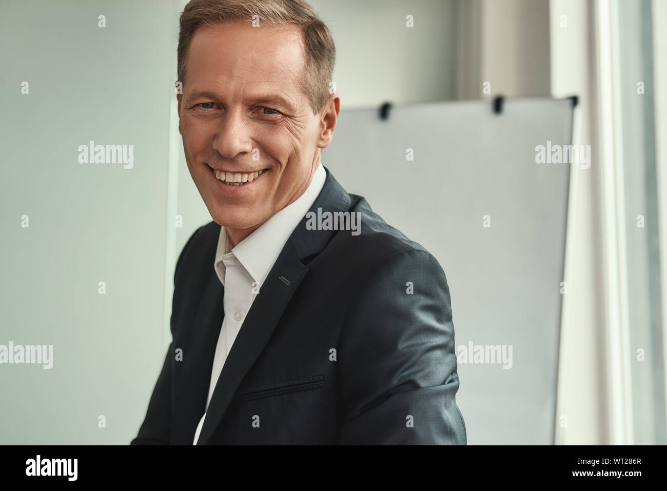 Erfolgreicher Geschäftsmann. Schön und heiter reifer Mann in formalen Verschleiß an Kamera schauen und lächeln, während sie im Büro zu sitzen. Geschäftsleute Stockfoto
