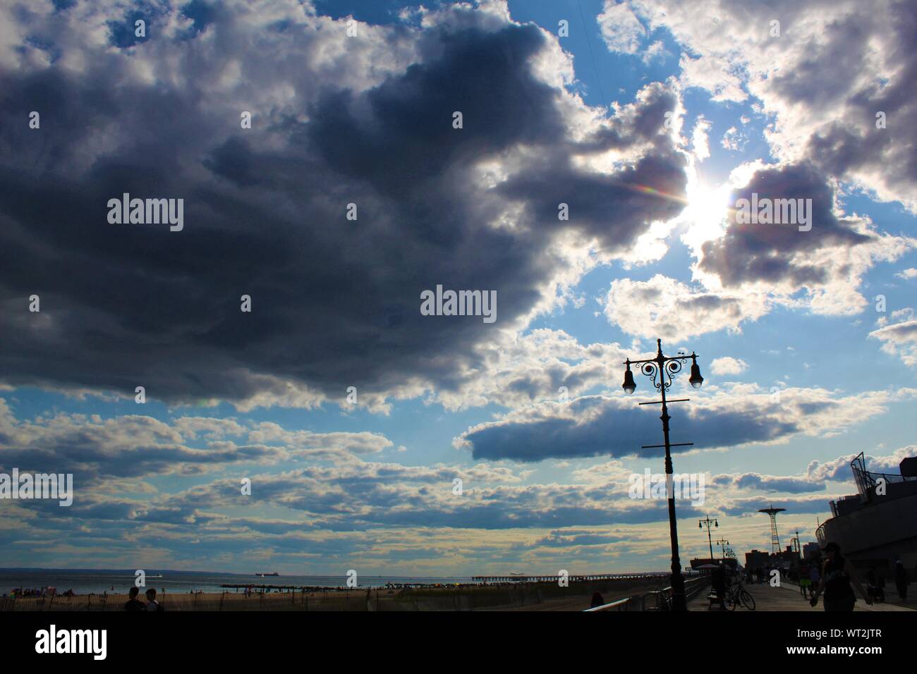 Sonne bricht durch bewölkter Himmel im Sommer an der Strandpromenade von Coney Island. Stockfoto