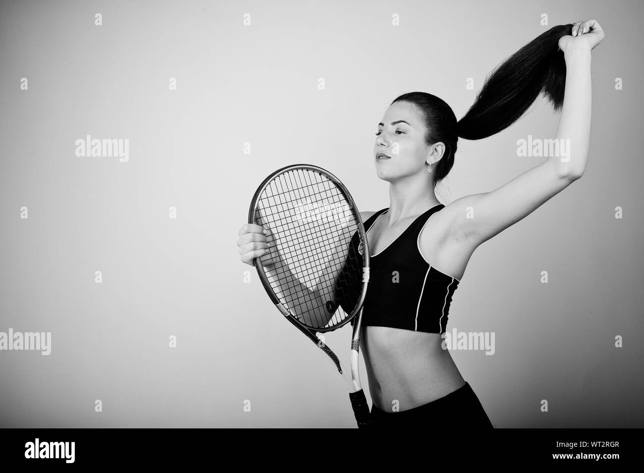 Schwarz-weiß-Porträt der schönen jungen Frau Spieler in Sport Kleidung, Tennisschläger, während gegen den weißen Hintergrund stehen. Stockfoto