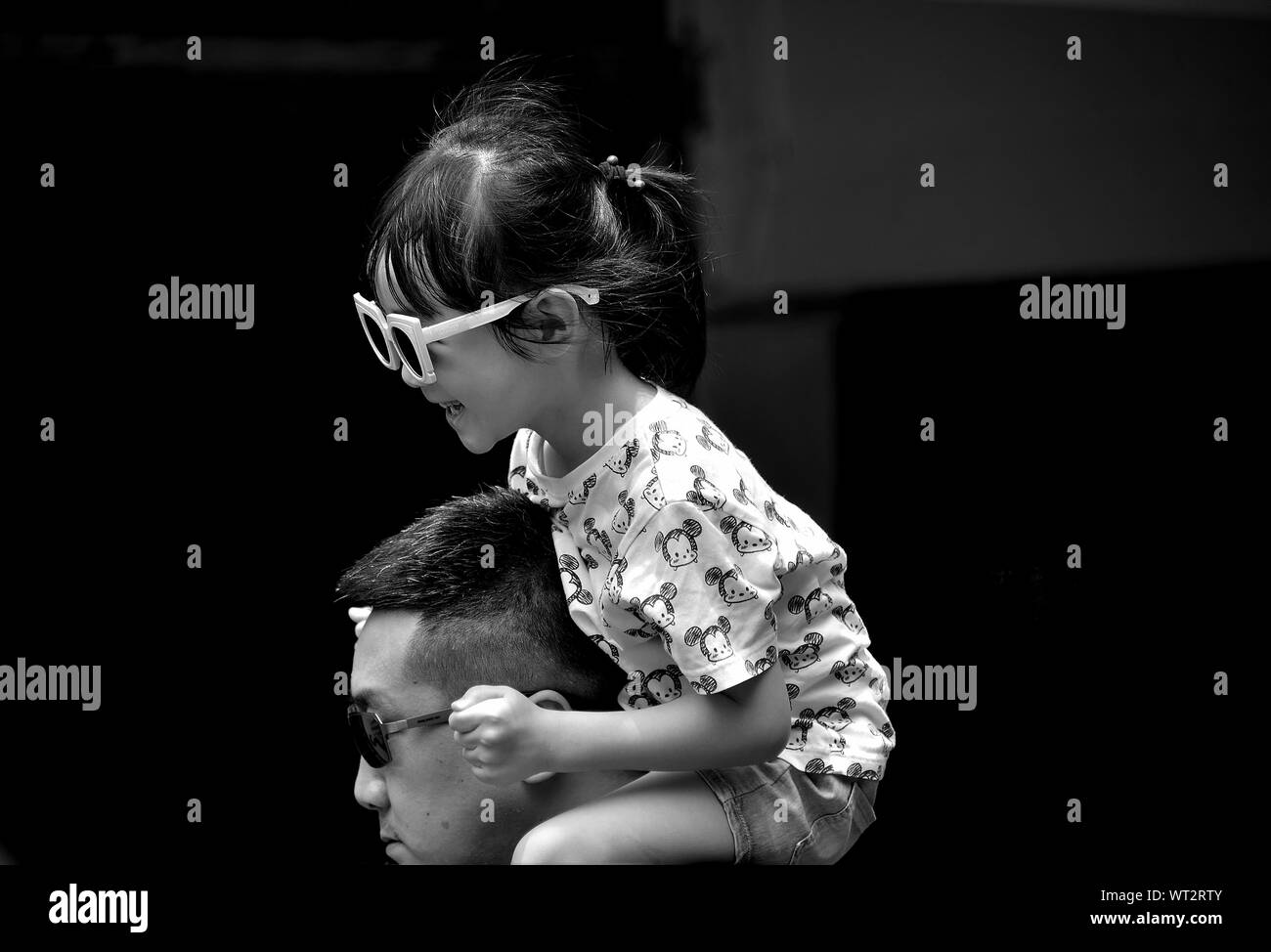 Junge chinesische Mädchen lachen und Reiten auf die Schulter ihres Vaters in natürlichen Portrait in Schwarz und Weiß Stockfoto