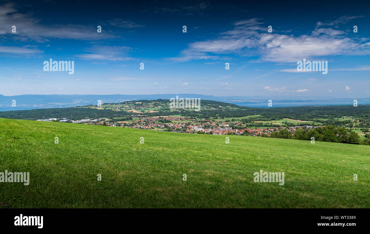 Stadt Landschaft in die Berge, Hügel, Felder, Wälder, grüne Wiesen, Seen in der Ferne und blauer Himmel mit Wolken. Stadt Bons-en-Chablais in Frankreich. Stockfoto