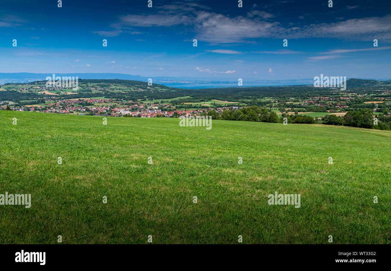 Stadt Landschaft in die Berge, Hügel, Felder, Wälder, grüne Wiesen, Seen in der Ferne und blauer Himmel mit Wolken. Stadt Bons-en-Chablais in Frankreich. Stockfoto