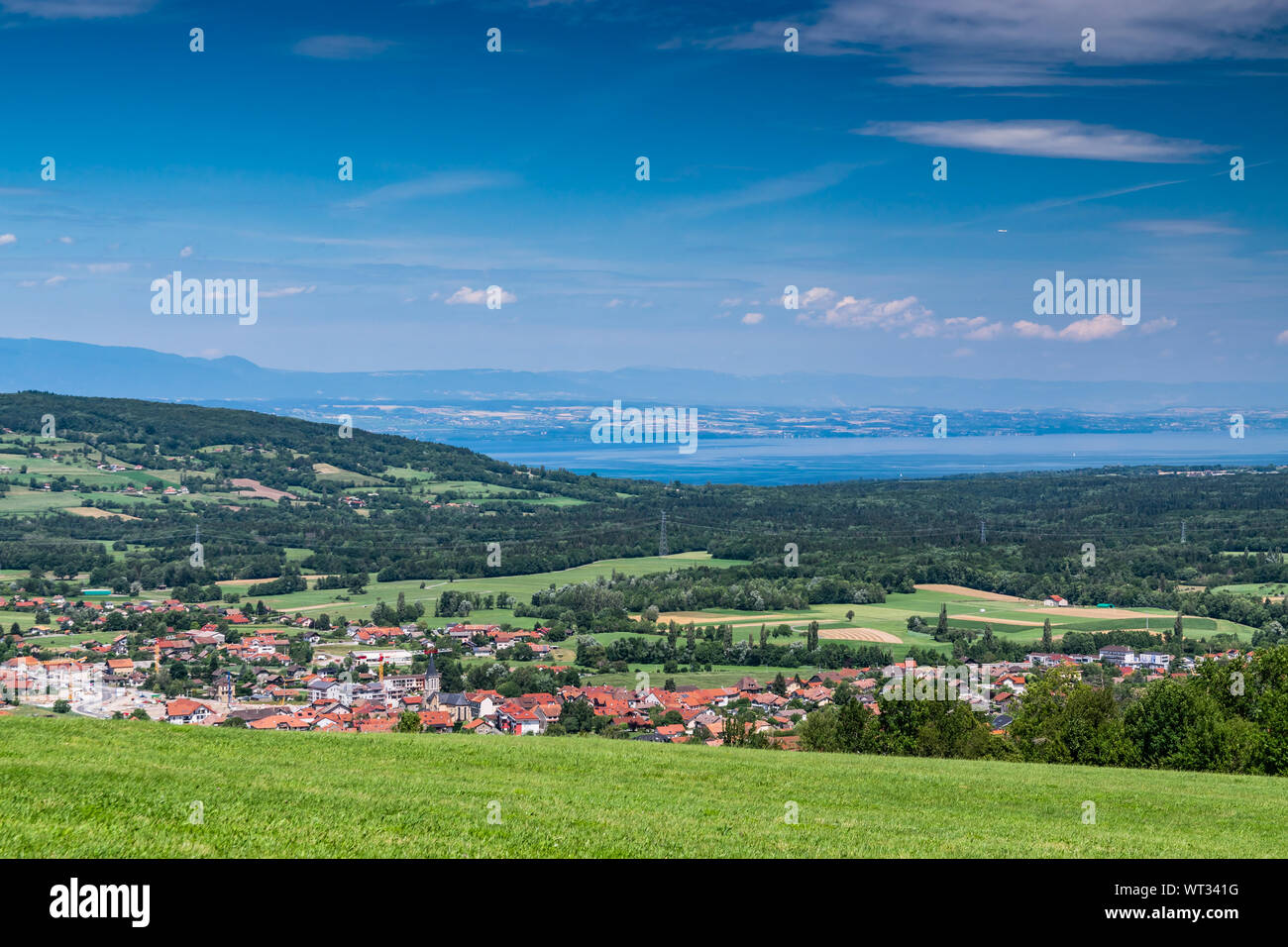 Stadt Landschaft in die Berge, Hügel, Felder, Wälder, grüne Wiesen, Seen in der Ferne und blauer Himmel mit Wolken. Stadt Bons-en-Chablais in Frankreich. Stockfoto