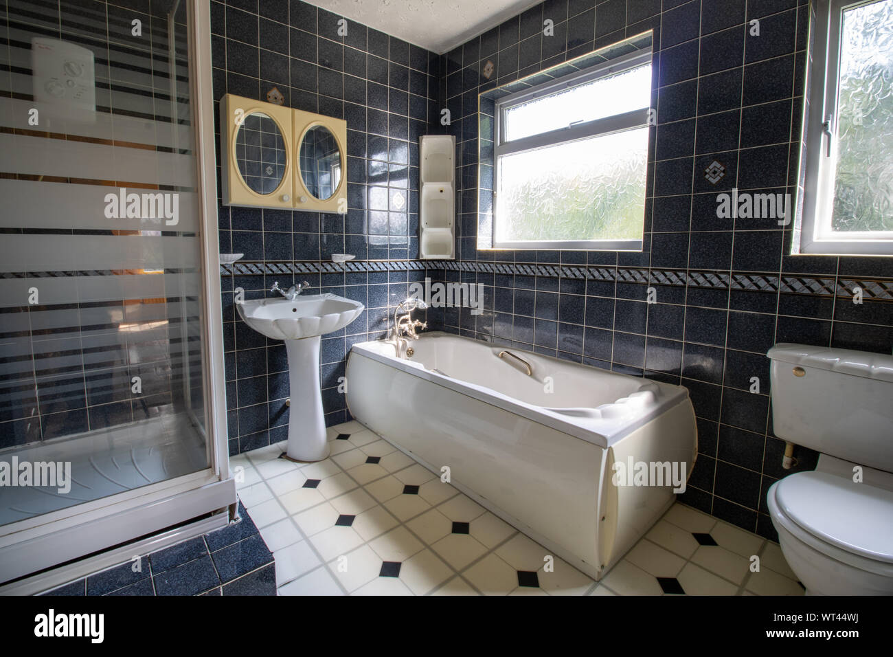 Eine alte 80er Stil Badezimmer, typisch britischen alten Stil Badezimmer  zeigt eine klassische Perle geformte Badewanne, Wc und  Waschbecken/Waschbecken mit schwarzen Fliesen eine Stockfotografie - Alamy