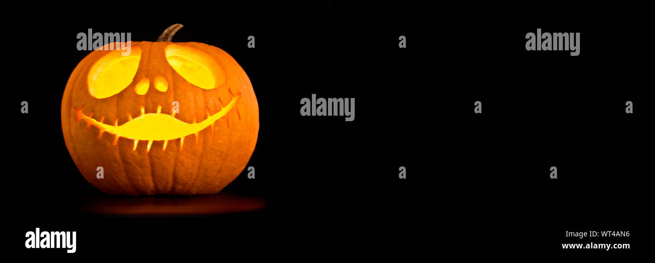 Beleuchtete Halloween Jack-o-Laterne Kürbis, schwarzer Hintergrund mit Panoramablick Platz kopieren Stockfoto